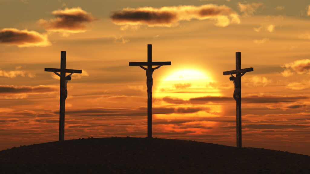 The silhouette of three crosses standing on a hill against a glorious sunset.